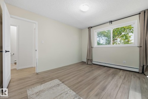 Spacious room featuring wood-finish flooring, a large window with white trim, and light-colored walls - 105 16428 109 Street, Edmonton, AB 