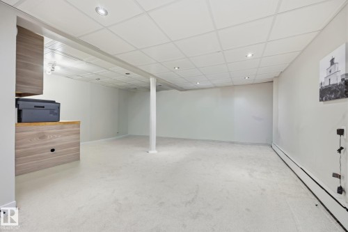Spacious finished basement featuring light-toned carpeting, a drop ceiling with recessed lighting, and a built-in wood-finish cabinet with an integrated countertop - 105 16428 109 Street, Edmonton, AB 