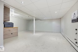 Spacious finished basement featuring light-toned carpeting, a drop ceiling with recessed lighting, and a built-in wood-finish cabinet with an integrated countertop - 