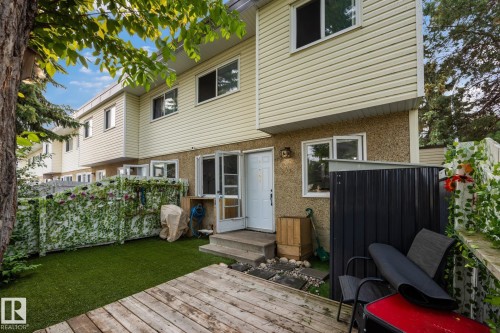 Private outdoor space featuring a wood-finish deck, artificial turf, and a white privacy fence with green vine accents - 105 16428 109 Street, Edmonton, AB 