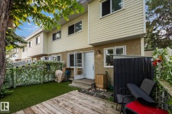 Private outdoor space featuring a wood-finish deck, artificial turf, and a white privacy fence with green vine accents - 