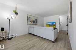 Spacious living area featuring light wood-finish flooring, white walls, and baseboard heating - 
