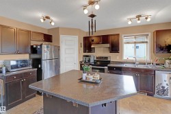 Kitchen featuring a central island with a speckled countertop, dark wood-finish cabinetry, stainless steel appliances, and track lighting fixtures - 