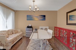 Spacious room featuring wood-finish flooring, a contemporary chandelier, and ample natural light from a large window - 