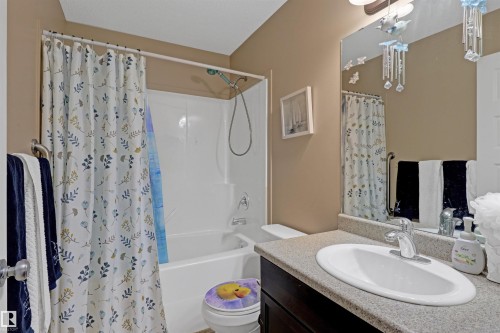 Bathroom featuring a white porcelain tub/shower combination, a vanity with a dark wood-finish cabinet, a light-colored countertop, and an integrated white oval sink - 1216 37C Avenue Nw, Edmonton, AB - Indoor Photo Showing Bathroom