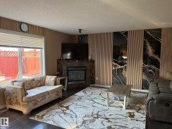 Living area featuring dark wood-finish flooring, a corner fireplace with a tile surround, and a picture window with horizontal blinds - 