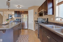 Kitchen featuring dark wood-finish cabinetry, stainless steel appliances, a double basin sink, and a multi-level island with an integrated countertop - 