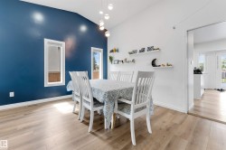 Vaulted ceiling dining area featuring a distinctive blue accent wall, wood-finish flooring, multiple windows with white trim, and a contemporary multi-bulb pendant light fixture - 