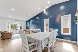 Vaulted ceiling with recessed lighting, light wood-finish flooring, and a dining area featuring a prominent blue accent wall - 
