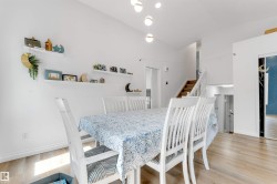 Dining area featuring wood-finish flooring, white walls, and a high ceiling with pendant lighting - 