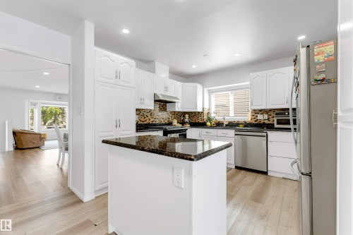 Kitchen featuring white cabinetry, dark stone countertops, stainless steel appliances, a mosaic tile backsplash, and light wood-finish flooring - 3332 43 Street, Edmonton, AB 