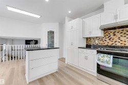 Contemporary kitchen featuring white cabinetry, dark countertops, and a patterned tile backsplash - 