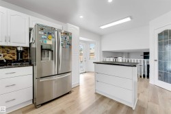Bright kitchen featuring white cabinetry, light wood-finish flooring, a mosaic tile backsplash, a central island with a dark countertop, and a glass-paneled door - 