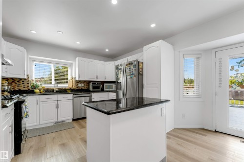 Spacious kitchen featuring white cabinetry, dark stone countertops, stainless steel appliances, wood-finish flooring, and direct outdoor access - 3332 43 Street, Edmonton, AB 
