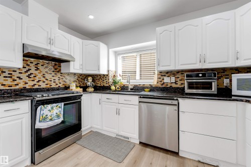 Kitchen featuring white cabinetry, dark speckled countertops, a mosaic tile backsplash, stainless steel appliances, and light wood-finish flooring - 3332 43 Street, Edmonton, AB 