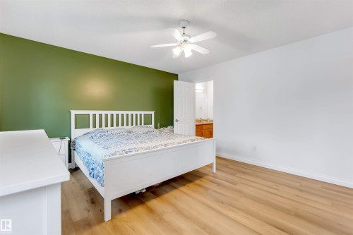 Spacious room featuring wood-finish flooring, a ceiling fan with integrated lighting, and a partial accent wall - 3332 43 Street, Edmonton, AB 