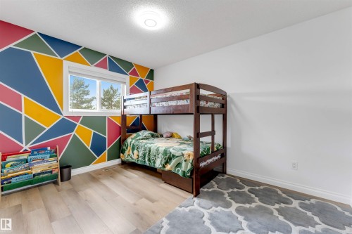 Room featuring a geometric accent wall with vibrant colors, light wood-finish flooring, and a white ceiling with a flush-mount light fixture - 3332 43 Street, Edmonton, AB 