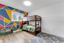 Room featuring a geometric accent wall with vibrant colors, light wood-finish flooring, and a white ceiling with a flush-mount light fixture - 