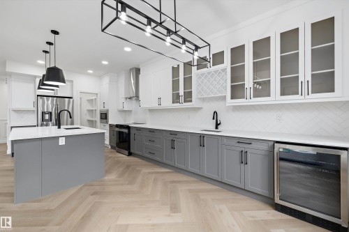 Gourmet kitchen featuring a spacious island with a sink, two-tone cabinetry, herringbone wood-finish flooring, stainless steel appliances, and a beverage cooler - 917 Elderberry Landing, Edmonton, AB 