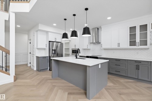 Modern kitchen featuring a large central island with a solid surface countertop, herringbone wood-finish flooring, stainless steel appliances, and two-tone cabinetry with white upper and gray lower units - 917 Elderberry Landing, Edmonton, AB 