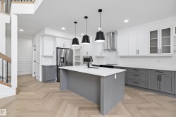 Modern kitchen featuring a large central island with a solid surface countertop, herringbone wood-finish flooring, stainless steel appliances, and two-tone cabinetry with white upper and gray lower units - 
