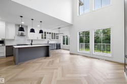 Modern kitchen featuring a large central island, white cabinetry, herringbone wood-finish flooring, and high ceilings with expansive windows - 