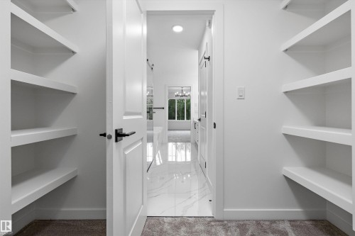 Walk-in closet featuring white shelving, light neutral carpet, and a white paneled door with black hardware - 917 Elderberry Landing, Edmonton, AB 