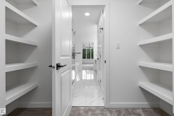 Walk-in closet featuring white shelving, light neutral carpet, and a white paneled door with black hardware - 