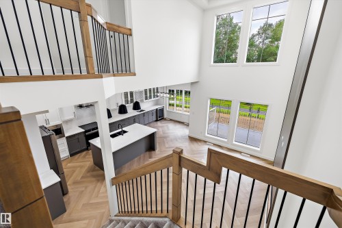Two-story living area with high ceilings, featuring a modern kitchen with a large island and herringbone wood-finish flooring - 917 Elderberry Landing, Edmonton, AB 