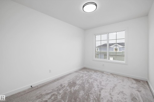Bright room featuring a multi-pane window with white trim, neutral carpet flooring, white walls, and a contemporary ceiling light fixture - 917 Elderberry Landing, Edmonton, AB 
