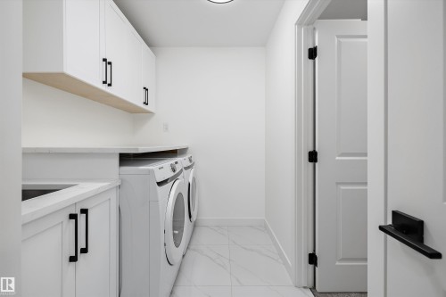 Dedicated laundry space featuring white cabinetry, light countertops, wood-finish shelving, a built-in sink, and marble-look floor tiling - 917 Elderberry Landing, Edmonton, AB 