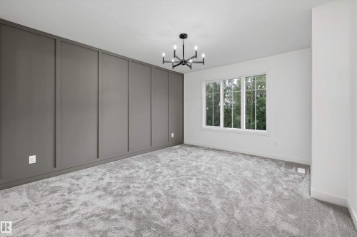 Room featuring a dark gray accent wall with vertical paneling, light gray carpeting, and a modern black chandelier - 917 Elderberry Landing, Edmonton, AB 