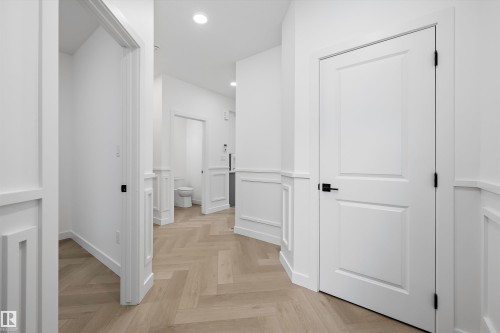 Hallway featuring herringbone wood-finish flooring, wainscoting, recessed lighting, and white paneled doors with matte black hardware - 917 Elderberry Landing, Edmonton, AB 