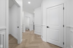 Hallway featuring herringbone wood-finish flooring, wainscoting, recessed lighting, and white paneled doors with matte black hardware - 