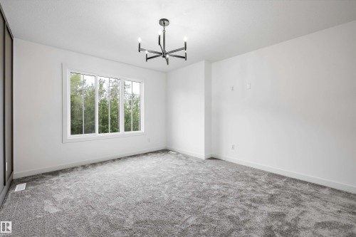 Spacious interior room featuring a multi-pane window, suspended four-light chandelier, light gray carpeting, crisp white walls, and white baseboards - 917 Elderberry Landing, Edmonton, AB 