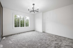 Spacious interior room featuring a multi-pane window, suspended four-light chandelier, light gray carpeting, crisp white walls, and white baseboards - 