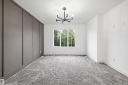 Room featuring a modern black chandelier, a large white-framed window, textured gray carpeting, a paneled accent wall, and clean white walls - 
