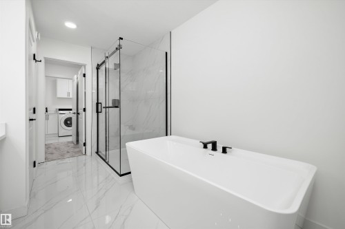 Modern bathroom featuring a freestanding tub with matte black fixtures, a glass-enclosed shower with black framing, and large-format tile flooring - 917 Elderberry Landing, Edmonton, AB 