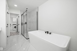 Modern bathroom featuring a freestanding tub with matte black fixtures, a glass-enclosed shower with black framing, and large-format tile flooring - 
