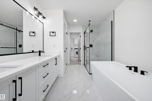 Contemporary bathroom featuring a freestanding soaking tub with matte black fixtures, a glass-enclosed shower, a dual vanity with white cabinetry and quartz countertops, and marble-look floor tiling - 917 Elderberry Landing, Edmonton, AB 