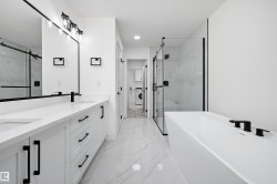Contemporary bathroom featuring a freestanding soaking tub with matte black fixtures, a glass-enclosed shower, a dual vanity with white cabinetry and quartz countertops, and marble-look floor tiling - 