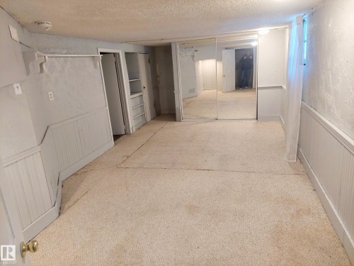 Carpeted room featuring white wainscoting, built-in shelving, mirrored closet doors, and a single window - 11238 123 Street, Edmonton, AB 