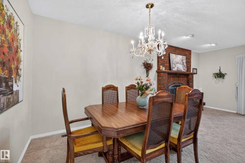 Dining area featuring a crystal chandelier, a brick fireplace with a wood mantle, and light-colored walls - 17603 85 Avenue Nw, Edmonton, AB 