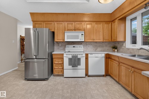 Kitchen featuring light wood cabinetry, stone-look tile flooring, and a stainless steel refrigerator - 17603 85 Avenue Nw, Edmonton, AB 