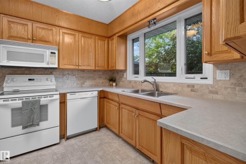 Kitchen featuring natural wood cabinetry, light-toned countertops, a stainless steel double sink, and a tiled backsplash - 17603 85 Avenue Nw, Edmonton, AB 