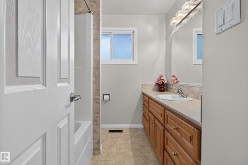 Bathroom featuring a wood-finish vanity with a single basin sink, a large mirror, and a window for natural light - 17603 85 Avenue Nw, Edmonton, AB 