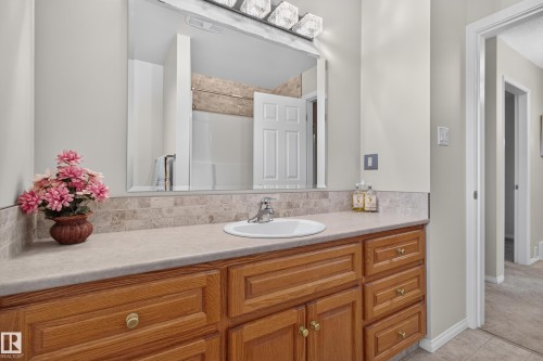 Bathroom vanity featuring a light-toned countertop with an integrated sink, a tiled backsplash, and wood-finish cabinetry with brass-toned hardware - 17603 85 Avenue Nw, Edmonton, AB 