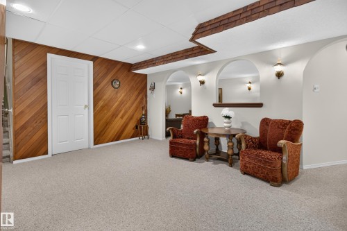 Carpeted room featuring a wood-paneled wall, white paneled door, and archway openings with integrated wall sconces - 17603 85 Avenue Nw, Edmonton, AB 