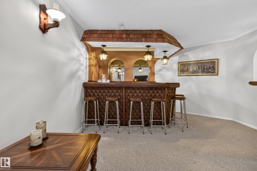 Built-in bar featuring a tufted leatherette facade, three pendant lights, a mirrored back wall, and a shingle-style roof accent - 17603 85 Avenue Nw, Edmonton, AB 