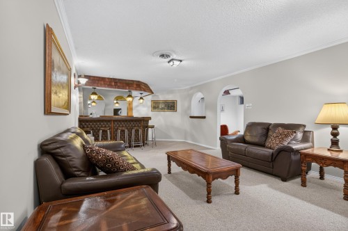 Spacious living area featuring light gray walls, plush carpeting, and a built-in bar with pendant lighting and textured wood paneling - 17603 85 Avenue Nw, Edmonton, AB 